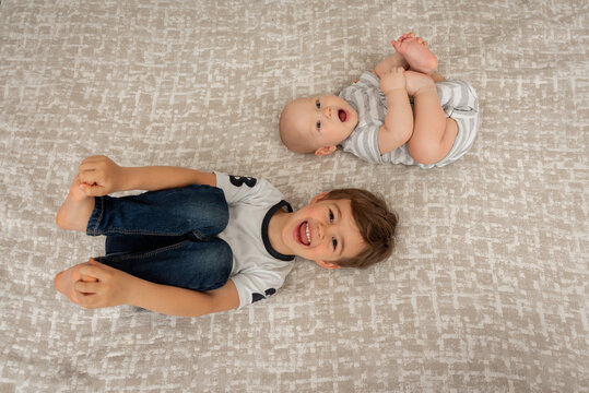 Two brothers lie on the bed and look up, smiling. View from above. Two little boys lying in pajamas on the bed, on their backs. Baby boy and his younger brother together on the bed