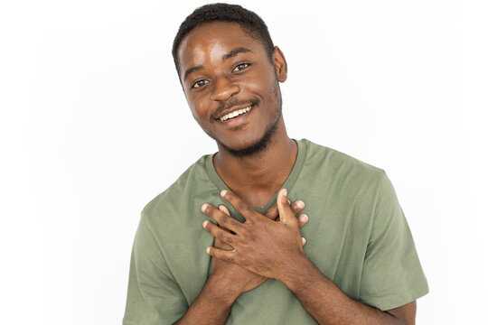 Pleased young man smiling from hearing compliment. Male African American model in green T-shirt looking happy and satisfied holding hands on his chest. Emotions, satisfaction concept