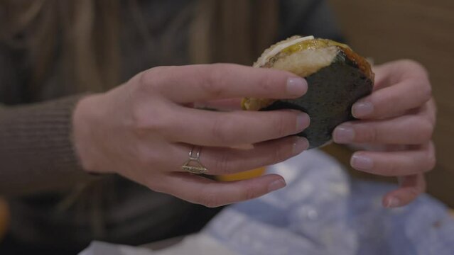 This video shows a caucasian woman picking up and eating a fast food rice bun Japanese burger.