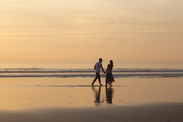 Loving couple walking on beach at sunset. Man and woman in casual clothes strolling along water at dusk. Love, family, nature concept