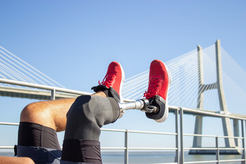 Close-up of legs of man with disability training. Sporty man doing morning exercises on bridge over...