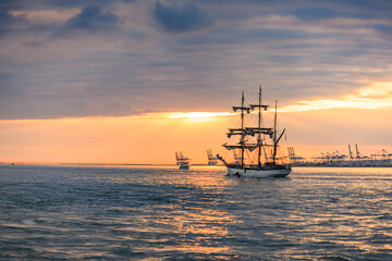 HONFLEUR, NORMANDY, FRANCE: Armada 2019 Grande Parade, tall ship Le Français sailing away in the Seine Estuary, in front of Le Havre harbour, with setting sun reflection in the sea - obrazy, fototapety, plakaty