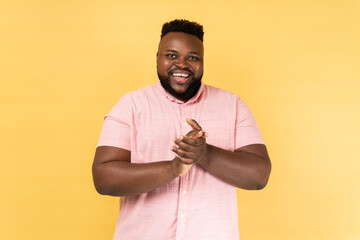 Portrait of positive friendly man wearing pink shirt standing with palms together, applauding,...