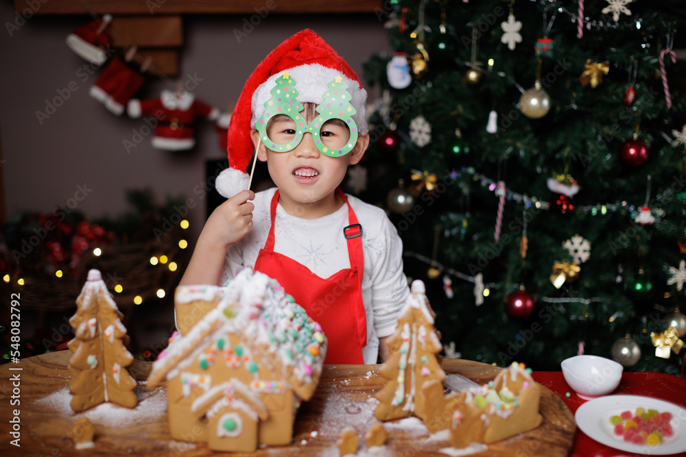 Wall mural young girl wearing santa hat was decorating gingerbread house for celebrating christmas at home