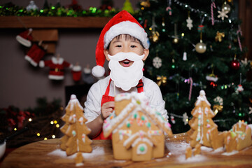 young girl wearing Santa hat was decorating gingerbread house for celebrating Christmas at home