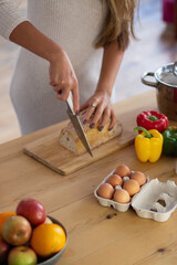 Close-up of female hands cutting loaf of bread for dinner. Careful wife holding bread on wooden board cutting it preparing meal for family to eat. Useful home food and healthy lifestyle concept