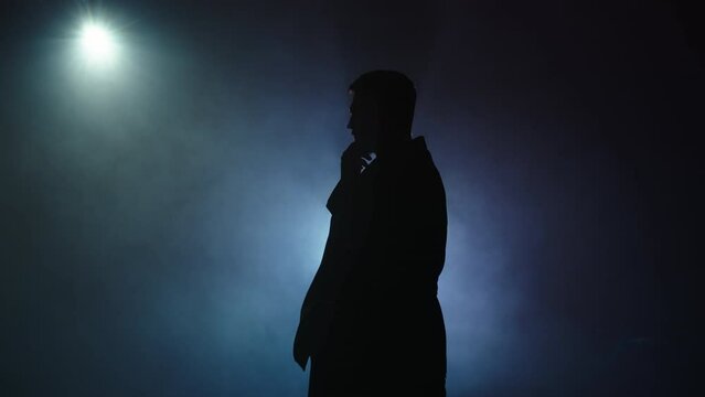 Silhouette of a man in a suit leaves the stage 4K. Mystical atmosphere, smoke, spotlight. Person in the dark