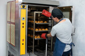 Baker in thermal gloves taking out the baked croissants.