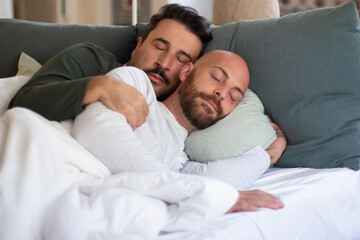 Obraz na płótnie Canvas Homosexual men hugging while sleeping in bed in morning. Medium shot of peaceful bearded gays in pajamas resting on weekend, lying in bed with closed eyes. LGBT, love, sleep cycle concept