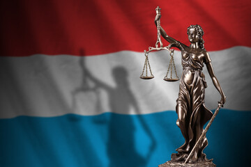 Luxembourg flag with statue of lady justice and judicial scales in dark room. Concept of judgement...