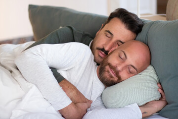 Homosexual couple sleeping in bed in morning and hugging. Peaceful handsome men in pajamas lying with closed eyes under blanket, resting on weekend. LGBT, love, sleep cycle concept