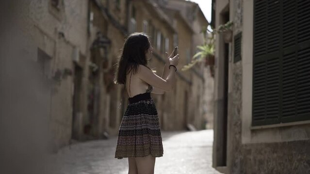 Young woman takes a photo with a smartphone in an empty rustic street. 