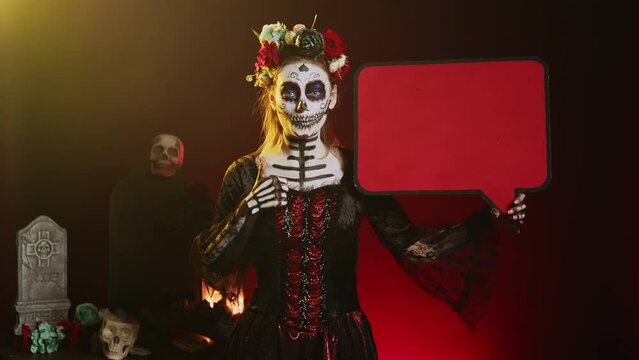 Holy lady of death holding speech bubble with skull make up and crown of roses, having creepy mysterious look. Woman using isolated copyspace template on cardboard, santa muerte advertisement.