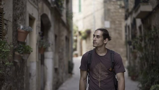Spanish athletic boy crosses an empty rustic street and looks at camera. 
