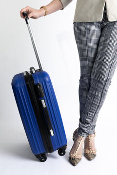 Lower half body of a girl dressed as an executive standing cross-legged holding a blue travel suitcase, on a white background