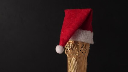 Champagne bottle wearing christmas hat rotating on black background. New Year celebration - Powered by Adobe