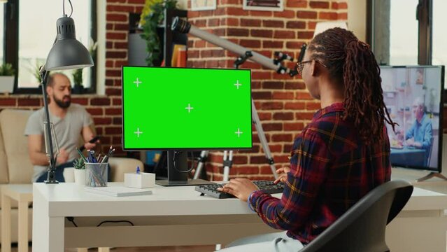 African american freelancer watching computer with greenscreen template, working with blank copyspace chromakey. Analyzing pc desktop with isolated mockup background on monitor in office space.