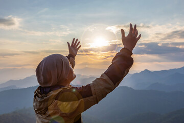 ํYoung male with hands open palm up praying to God on the mountain sunset background. - obrazy, fototapety, plakaty