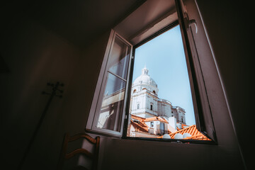 A wide-angle view from the dark domestic room through the opened window of a cathedral with a dome,...