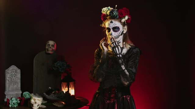 Young scary woman doing hush gesture to keep secret, wearing santa muerte costume and showing slience mute and secrecy sign with finger over lips. Holy dios de los muertos holiday.