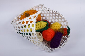 Hand-made and colorful crocheted vegetables in a basket against a white background