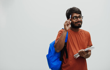 Confused indian student with blue backpack, glasses and notebook posing on gray background. The concept of education and schooling. Time to go back to school