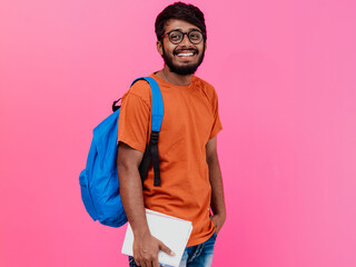  Indian student with blue backpack, glasses and notebook posing on pink background. The concept of education and schooling. Time to go back to school