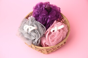 Wicker basket with colorful shower puffs on pink background, above view