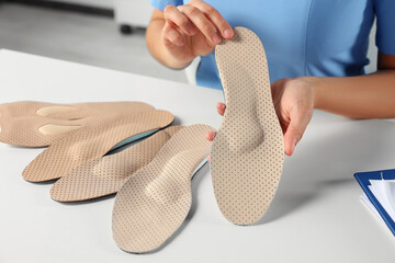 Female orthopedist showing insoles at table in hospital, closeup