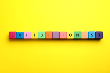 Word EXHIBITIONIST made with colorful cubes on yellow background, flat lay