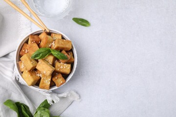Bowl with delicious fried tofu, basil and sesame seeds on white table, flat lay. Space for text
