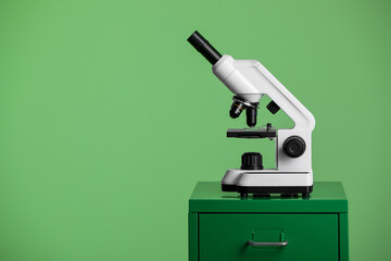 Modern medical microscope on lab drawer against green background, space for text