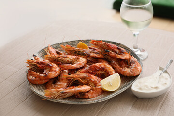 Plate of delicious cooked shrimps served with lemon, sauce and wine at table