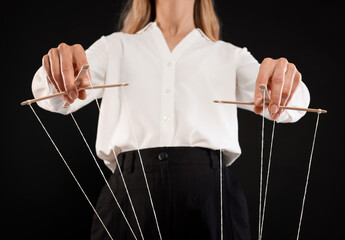 Woman in formal outfit pulling strings of puppet on black background, closeup