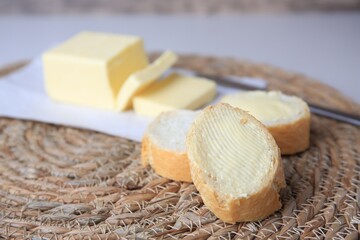 Tasty cut baguette with fresh butter on wicker mat, closeup