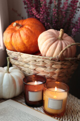 Beautiful heather flowers, burning candles, open book and wicker basket with pumpkins indoors