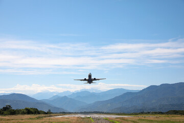 Naklejka na ściany i meble Modern white airplane landing on runway near mountains