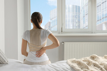 Woman with orthopedic corset sitting in bedroom, back view
