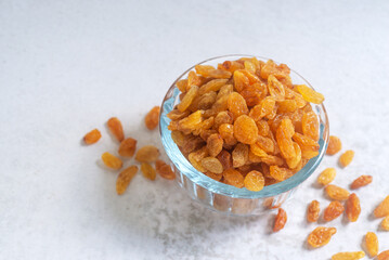Golden raisins (sultanas) in a glass bowl on white table background.