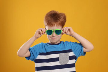 Cute little boy with sunglasses on yellow background