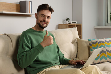 Handsome man with laptop sitting on sofa at home