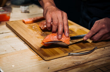 Close up of Chef cook hands chopping salmon fish for traditional Asian cuisine with Japanese knife. Professional Sushi chef cutting seafood japanese chefs are making salmon fish sashimi. dark tone