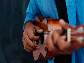 Indian young man in a blue shirt and glasses playing the guitar in front of the school blackboard