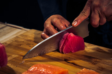 Close up of Chef cook hands chopping tuna fish for traditional Asian cuisine with Japanese knife....