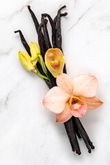 Dried vanilla sticks and orchid flower set up on marble background.