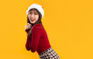 Young asian woman in red long sleeve t shirt wear santa hat posing smiling and wishing yellow background.