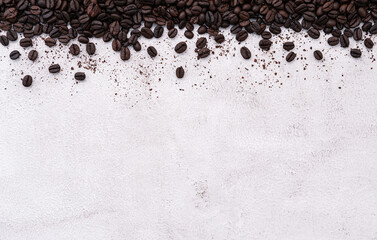 Dark roasted coffee beans setup on white concrete background with copy space.