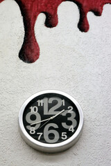 Reloj de pared sobre una pared blanca con gotas de pintura roja encima bajando del techo