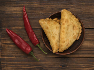 Two red pepper pods and fried pies on a wooden table.