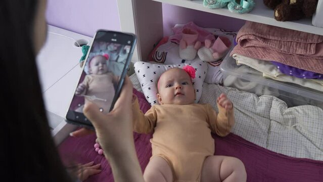 Young woman photographing her cute baby with a smart phone, infant girl lying on changing table, selective focus